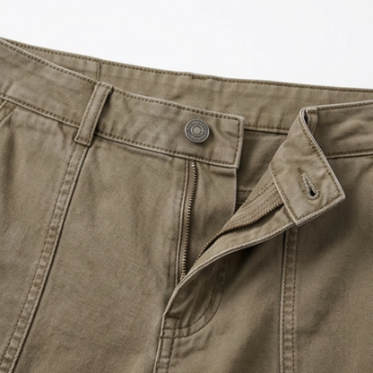 Warm khaki utility pants close-up with zipper fly, coin pocket, and metal logo patch