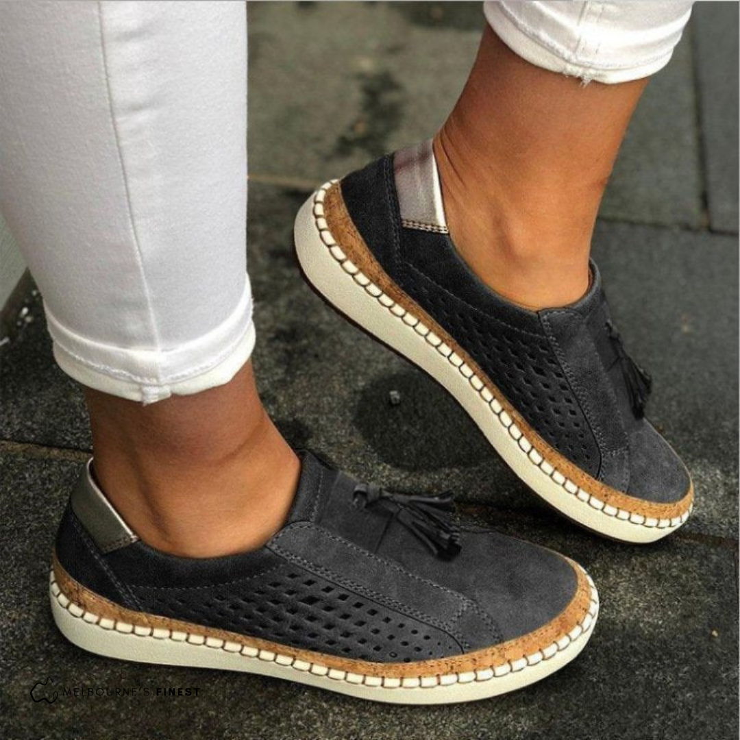 Orthopedic black slip-on shoes with perforated sides, tassel detail, and beige sole