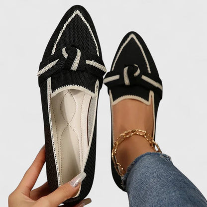 Black orthopedic loafers with white piping, lace bow and textured fabric upper.