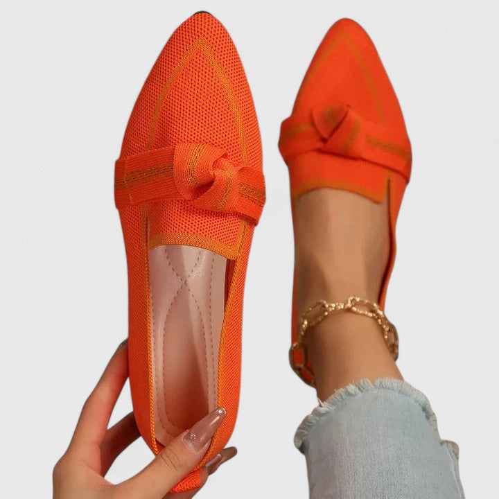 Orange orthopedic loafers with textured knit upper, lace bow and dark trim.